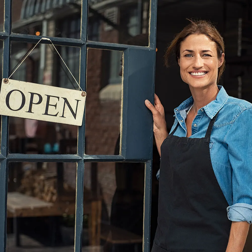 Smiling small business owner standing in the doorway of her shop beside an open sign