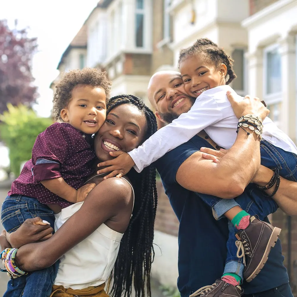 Smiling parents holding their two young children outside their home