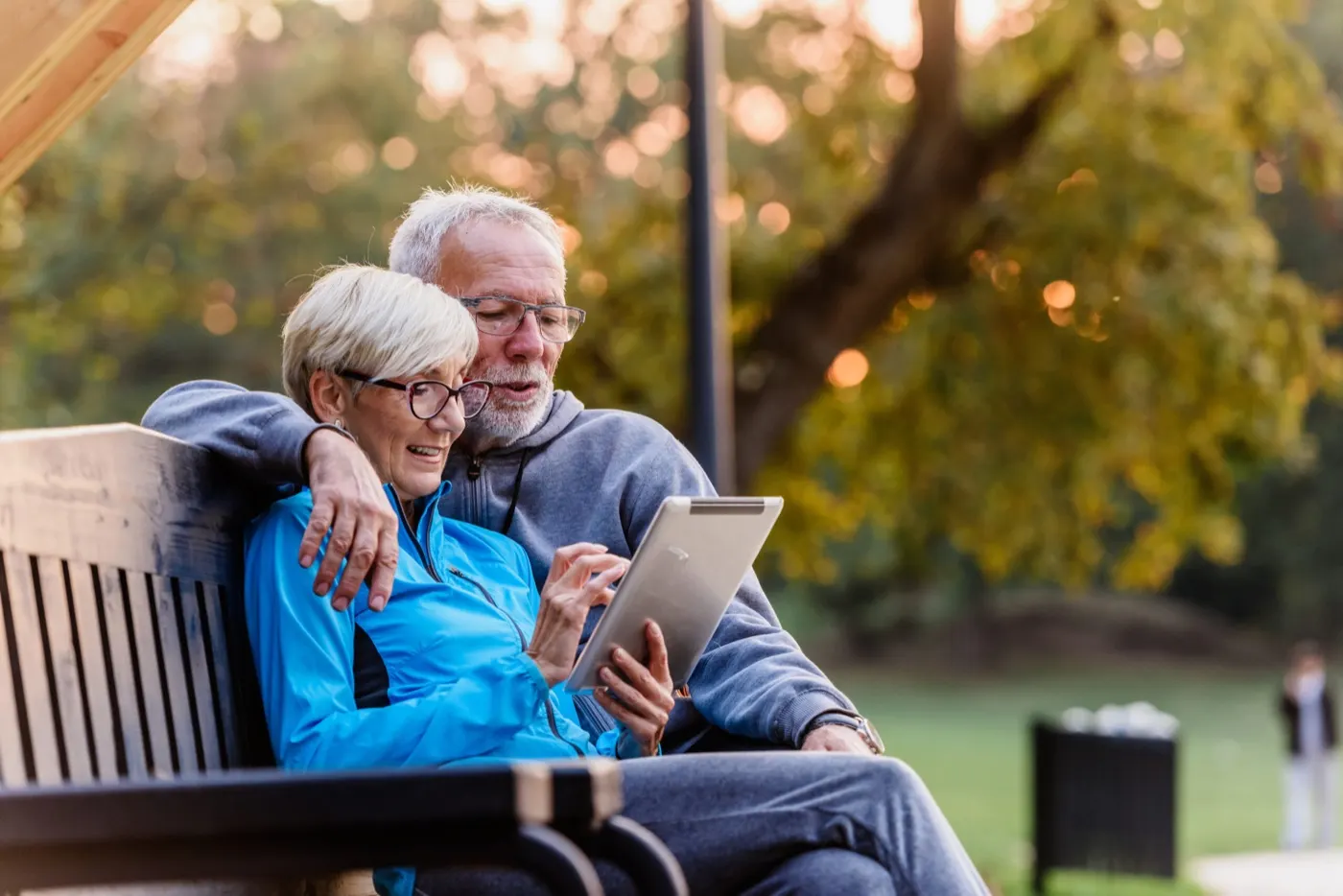 Smiling senior couple sitting on a park bench looking at a tablet